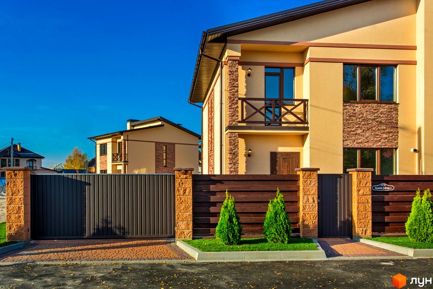 Котеджне містечко Злагода: двоповерхові будинки з кам'яним оздобленням та дерев'яними елементами, огороджені парканом з автоматичними воротами. Прибудинкова територія з газоном та туями.