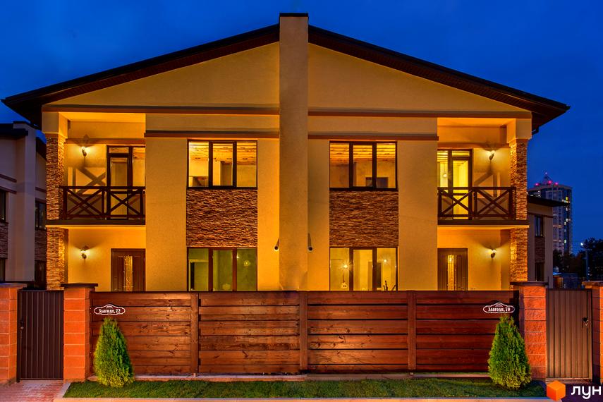 Котеджне містечко КМ Злагода: двоповерхові будинки з балконами та дерев'яним парканом. Навколо будинку доглянута територія з газоном та туями.