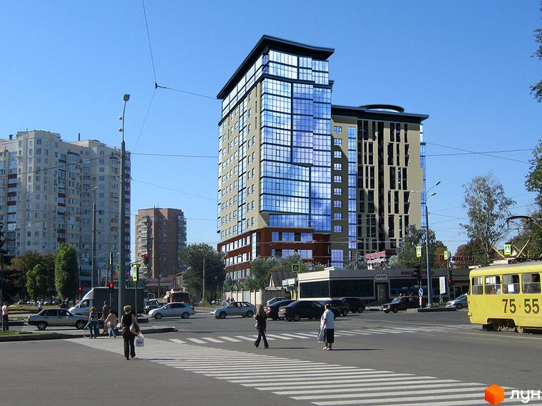 Житловий комплекс Кристал - це сучасна новобудова з панорамним склінням та оригінальною архітектурою. На зображенні видно фасад будівлі та прилеглу вулицю з транспортом.