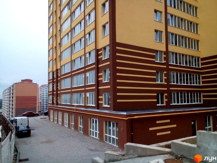 Багатоповерховий будинок Житлового комплексу Авіла з жовто-коричневим фасадом та білими вікнами. Перед будинком розташована вимощена територія з припаркованими автомобілями.