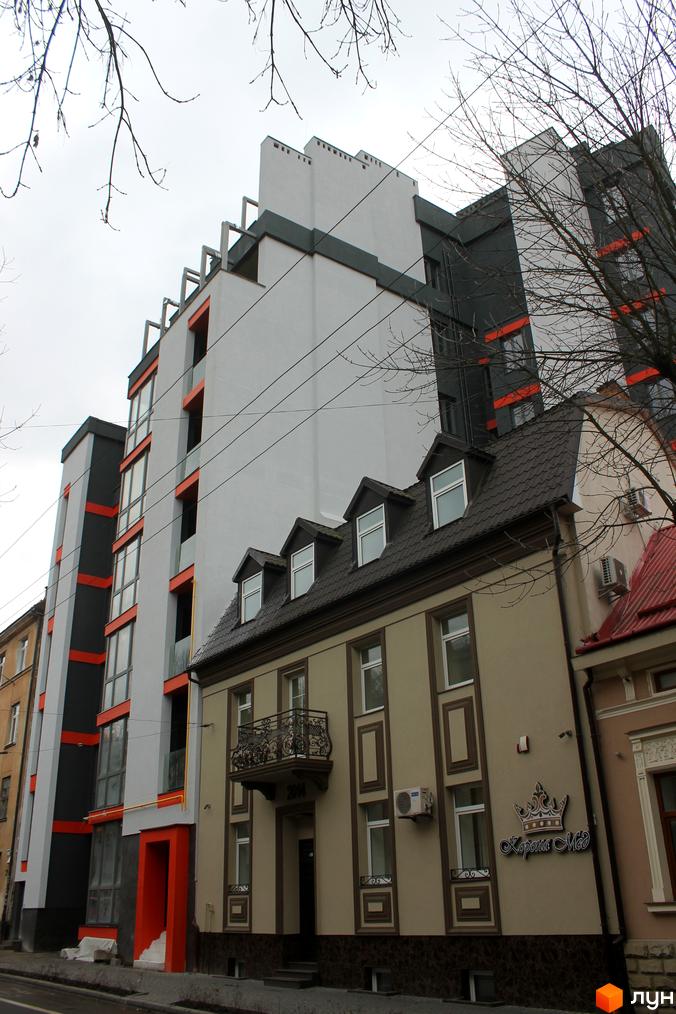 Новобудова на вул. Снопківська, 18а з сіро-білим фасадом, помаранчевими акцентами та великими вікнами. Поруч розташований малоповерховий будинок.