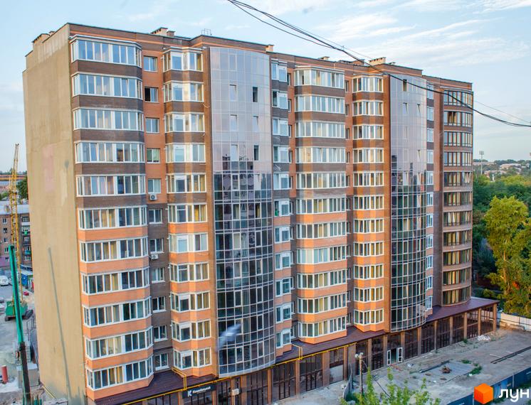 Новобудова ЖК Ковалівський з цегляним та скляним фасадом. Навколо будинку видно будівельні роботи та зелені насадження.