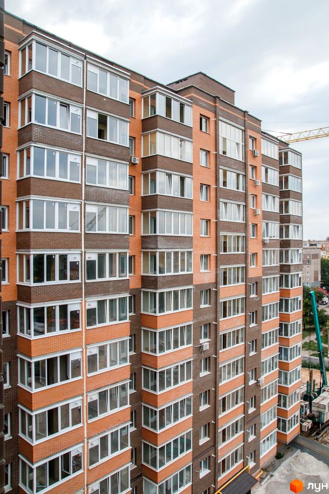 Житловий комплекс Ковалівський – це багатоповерхова цегляна новобудова з численними вікнами та балконами. На фоні видно будівельний кран.