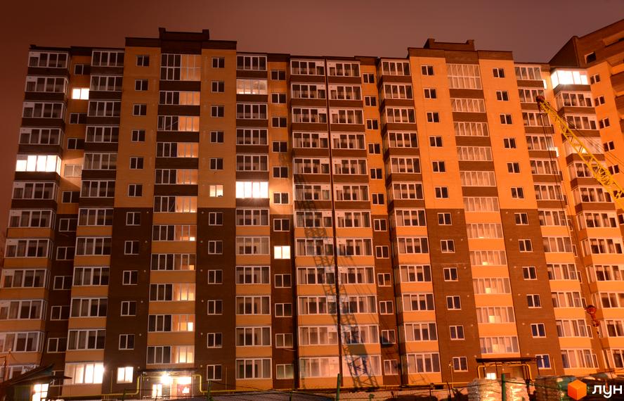 Житловий комплекс Зарічний: багатоповерховий будинок з численними освітленими вікнами вночі. На фасаді чергуються темні та світлі цегляні секції.