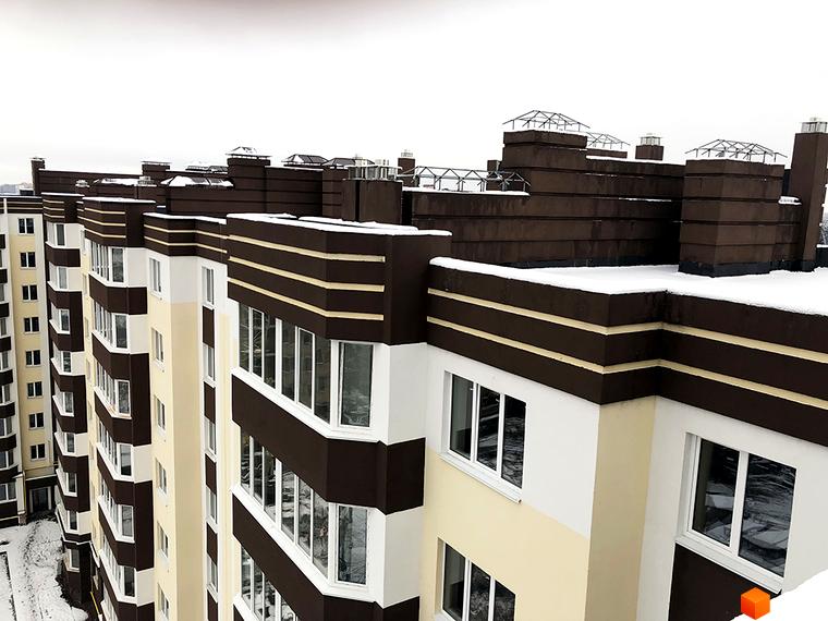 Зовнішній вигляд новобудови ЖК Домашній з коричнево-білими фасадами та вікнами. Будівля вкрита снігом, що свідчить про зимовий період.