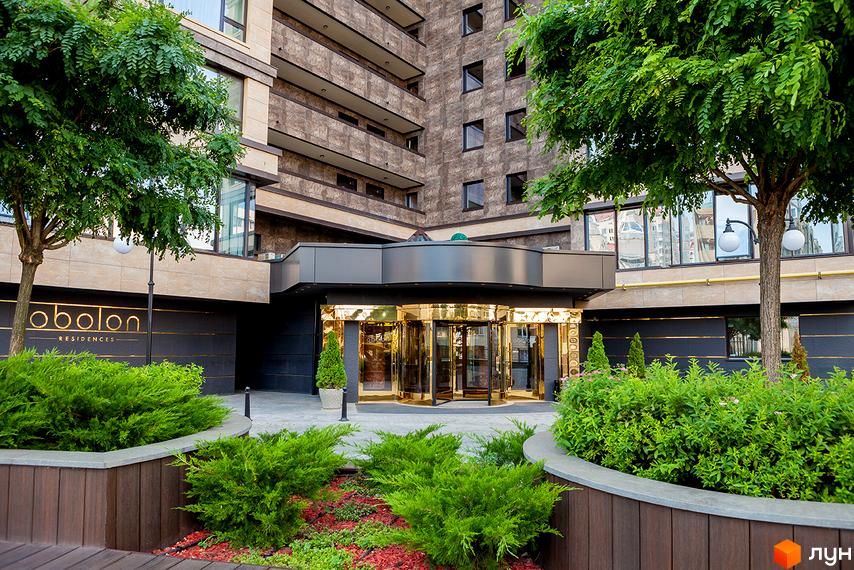 Новобудова Obolon Residences: багатоповерхова будівля з коричневим фасадом, золотим входом та доглянутою прибудинковою територією з зеленими насадженнями.