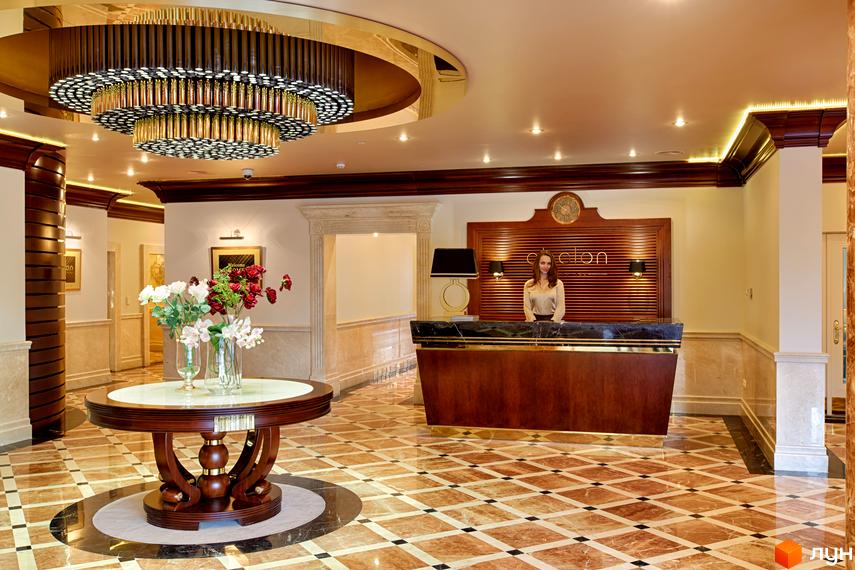 Лобі Житлового комплексу Obolon Residences: рецепція з адміністратором, круглий стіл з квітами, мармурова підлога та велика люстра.