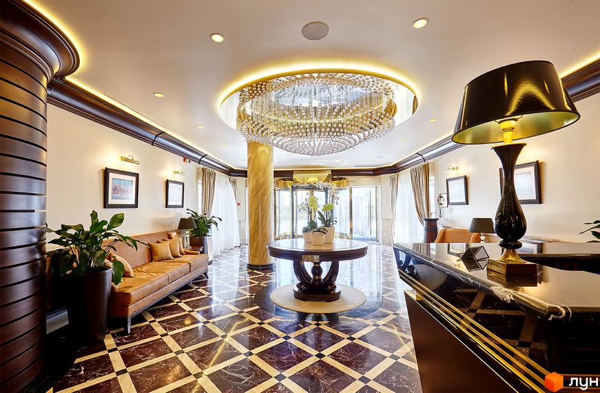 Просторий інтер'єр лобі Житлового комплексу Obolon Residences з кришталевою люстрою, мармуровою підлогою та дерев'яними елементами.