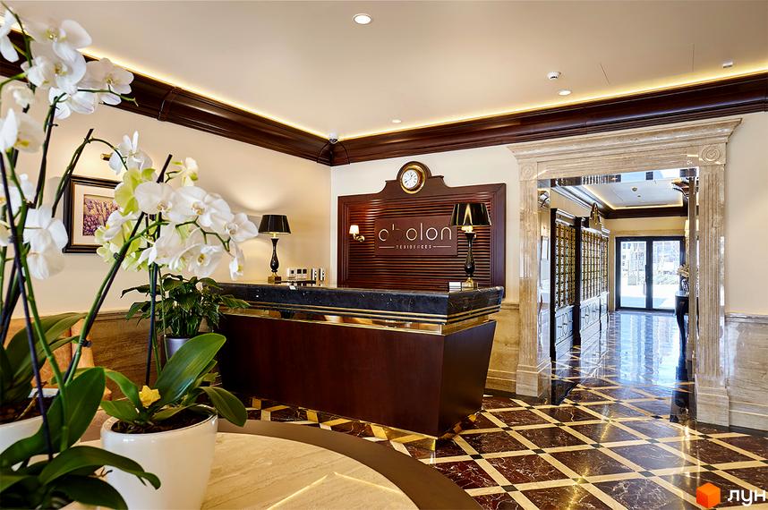 Лобі Житлового комплексу Obolon Residences з дерев'яною рецепцією, мармуровою підлогою та арковим проходом до коридору.