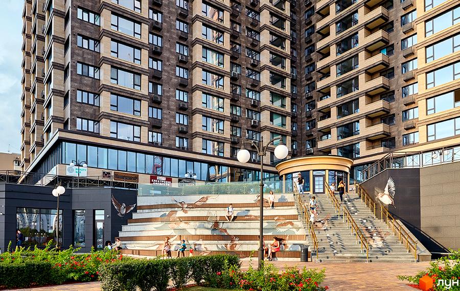 Obolon Residences - житловий комплекс з фасадом з темної та світлої плитки, балконами та великими вікнами. Прибудинкова територія з сходами, декорованими зображеннями птахів, та зонами відпочинку.