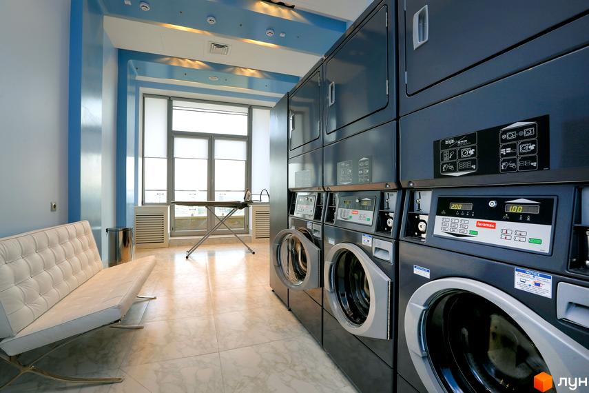 Простора пральня з пральними машинами, сушарками та місцем для прасування у Житловому комплексі Obolon Residences.