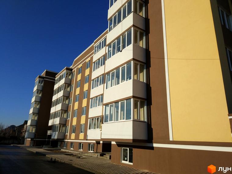 Зовнішній вигляд житлового комплексу Сучасний з коричнево-жовтим фасадом та численними балконами. Прибудинкова територія з бруківкою та дорогою.