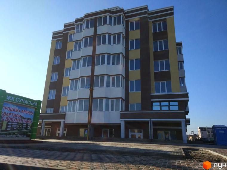 Зовнішній вигляд багатоповерхового будинку ЖК Сучасний з коричневими та жовтими фасадами. Поруч видно зелену вивіску з інформацією про продаж та оренду квартир.