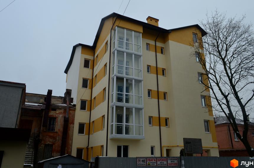 Зовнішній вигляд новобудови на вул. Корсунська, 4. Фасад будинку оздоблений жовтими та білими смугами, з панорамним скляним балконом. Навколо будівлі видно паркан та дерева.