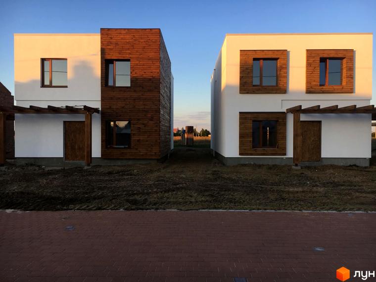 Котеджне містечко На Щасливій. Зовнішній вигляд двох будинків з дерев'яними елементами та білою штукатуркою. Перед будинками облаштована територія з червоною бруківкою та зеленими насадженнями.