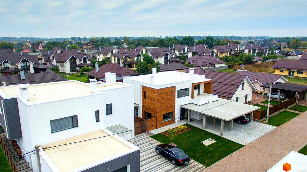 Котеджне містечко На Щасливій: сучасні будинки з коричневими дахами та доглянутими прибудинковими територіями. На території комплексу розташовані зелені газони, паркувальні місця та доріжки.