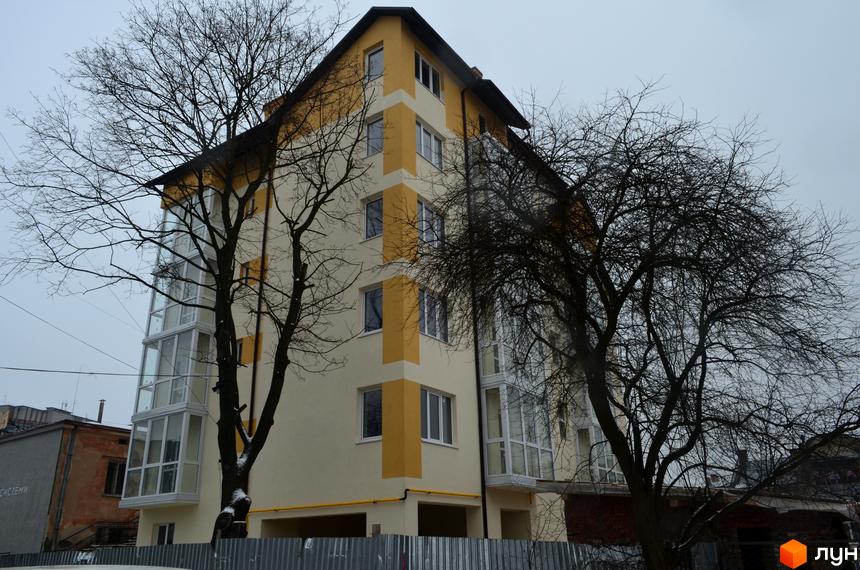 Новобудова на вул. Корсунська, 4. Багатоповерховий будинок з жовтими та білими елементами фасаду, скляними балконами та гострим дахом. Навколо будинку голі дерева.