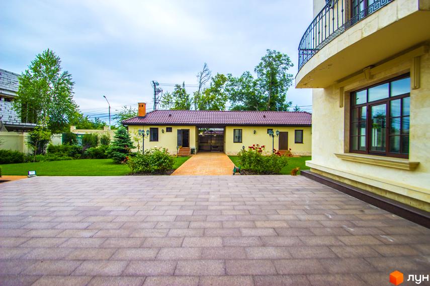 Клубний будинок „Ліон“ з жовтим фасадом, червоним дахом та доглянутою прибудинковою територією з газоном і квітами. На території є брукований двір та зелені насадження.