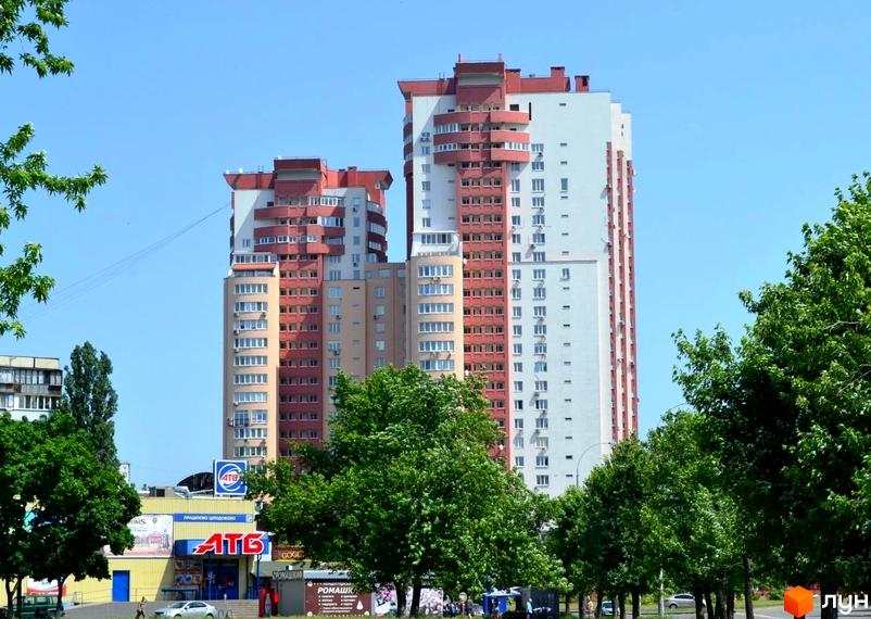 Дві висотні житлові будівлі за адресою вул. Тичини, 18б, з червоно-білими фасадами та округлими балконами. Поруч зелені дерева та супермаркет АТБ.