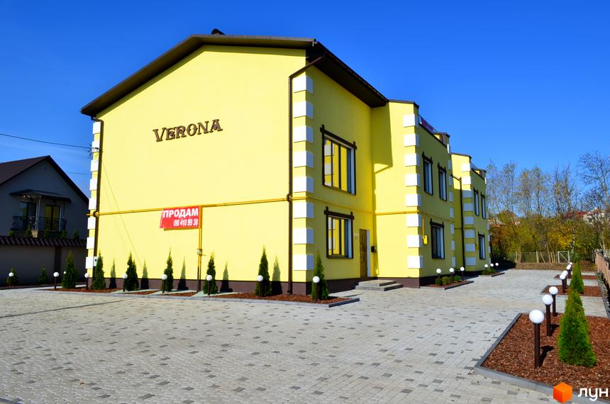 Таунхаус Verona жовтого кольору з білими декоративними елементами. Навколо будинку вимощена бруківкою територія з висадженими туями та ліхтарями.