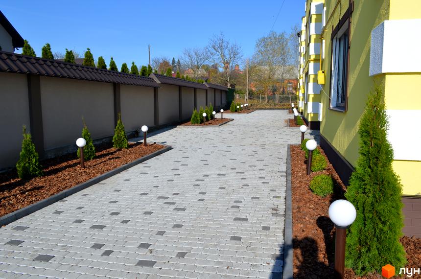 Таунхаус Verona: жовта будівля з білими декоративними елементами, вимощена доріжка та зелені насадження. Ознайомтеся з новобудовою.