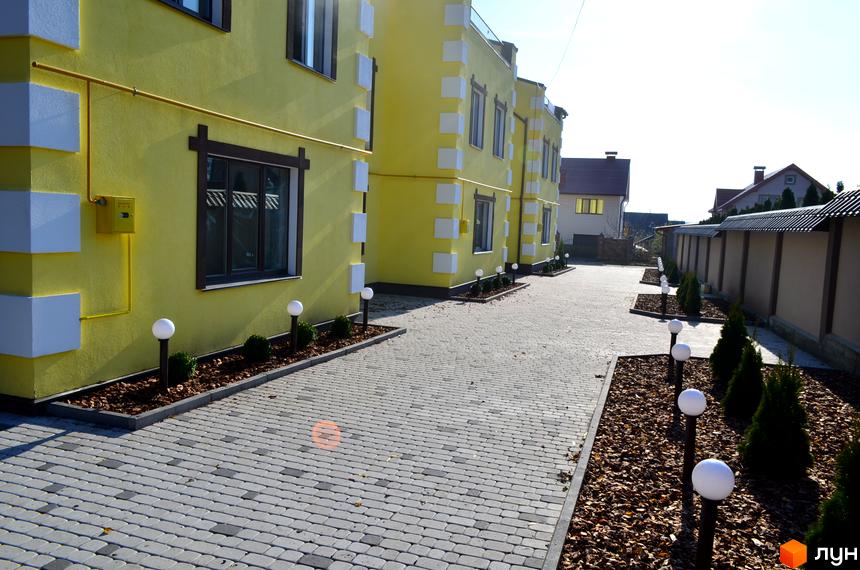 Таунхаус Verona з жовтим фасадом та білими елементами. Озеленена прибудинкова територія з бруківкою та ліхтарями.