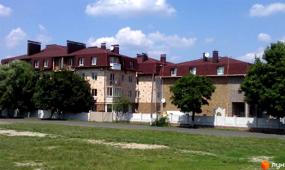 Житловий комплекс Молодіжний з червоною покрівлею та фасадом з каменю. Прибудинкова територія з зеленими насадженнями та огорожею.