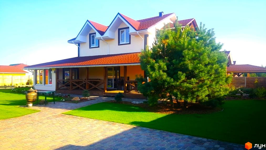 Котеджне містечко КМ Лісовий Хуторок: двоповерховий будинок з червоним дахом, верандою та доглянутою прибудинковою територією з газоном і бруківкою.