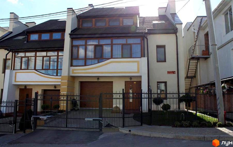 Зовнішній вигляд будинку у пров. Паневежиський (Пугачова), 2. Двоповерховий будинок з великими вікнами та коричневими дверима, перед будинком металева огорожа.