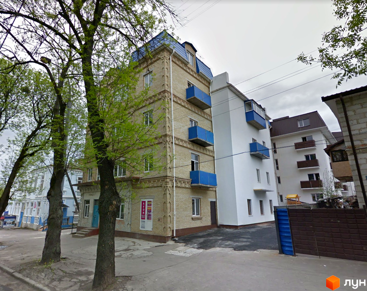 Житловий комплекс на вулиці Дубенська, 7. Фасад будинку оздоблений світлою цеглою та має сині балкони. Поруч розташовані дерева та проїжджа частина.