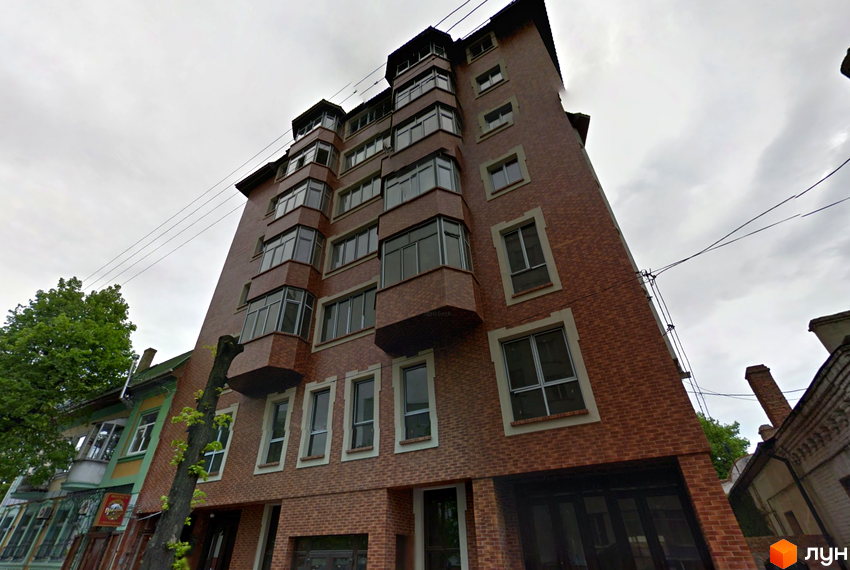 Зображення цегляного житлового комплексу на вул. Тиха, 4 / вул. 16-го Липня, з виступаючими балконами та вікнами.