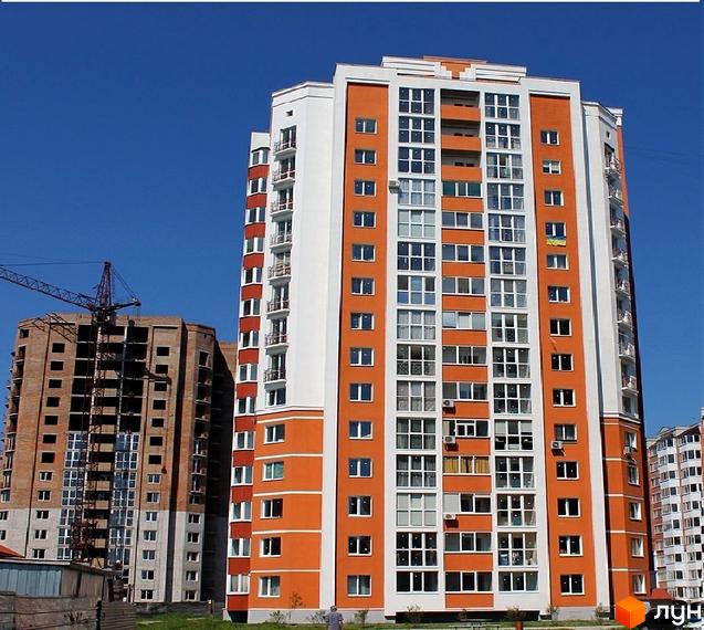Житловий комплекс на вул. Олександра Бідного, 18 з помаранчево-білим фасадом та скляними балконами. Поруч видно будівництво нового будинку.