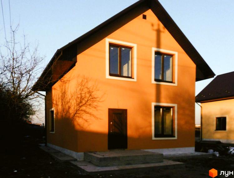 Котеджне містечко КМ Green House: двоповерховий будинок з помаранчевою штукатуркою та темним дахом, три вікна на фасаді, тінь від дерева на стіні. Поруч сусідній будинок, сонячний день.