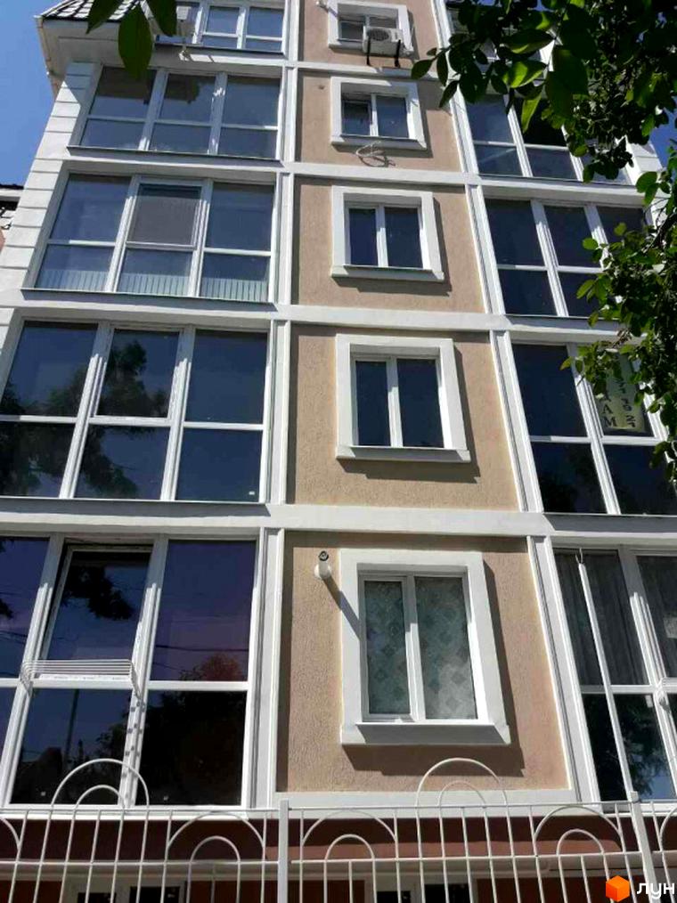 Фасад житлового комплексу Клубний з великими вікнами та білим оздобленням. Видно частину огорожі та зелені.