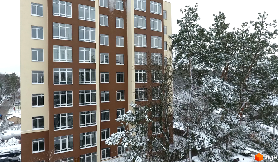 Житловий комплекс Green Life-2. Багатоповерховий будинок з великою кількістю вікон. Навколо будівлі ростуть дерева, вкриті снігом.