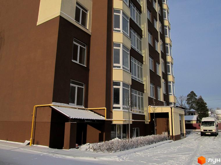 Багатоповерховий будинок ЖК Green Life-2 з великими вікнами. На прибудинковій території сніг, видно частину дороги та автомобіль.