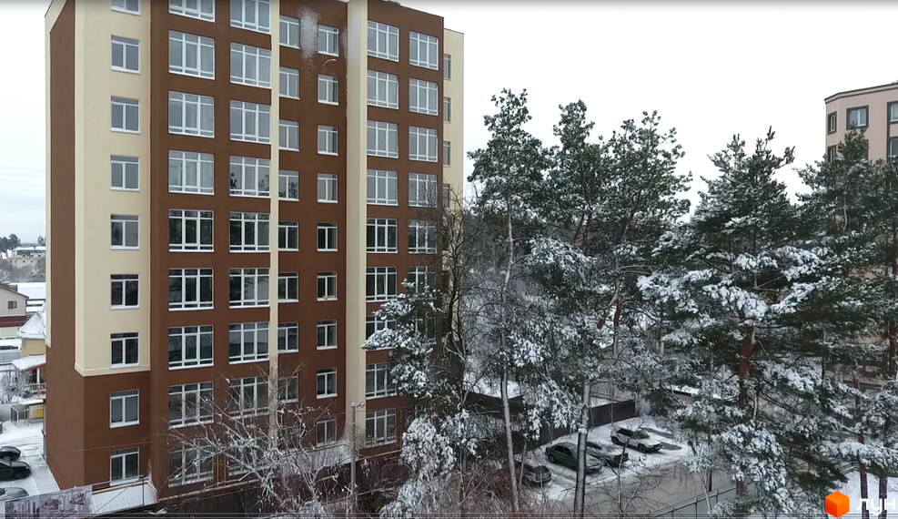 Висотна будівля Житлового комплексу Green Life-2 з великими вікнами. На передньому плані засніжені дерева та стоянка для автомобілів.