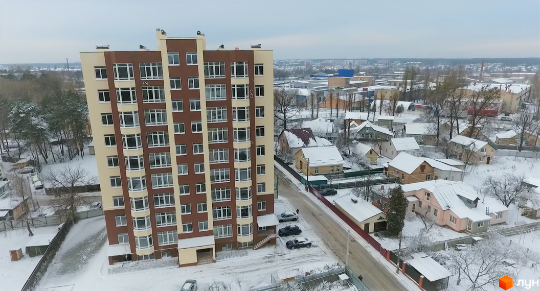 Висотна будівля ЖК Green Life-2 з великою кількістю вікон. Навколо будинку засніжена прибудинкова територія з невеликими будинками.