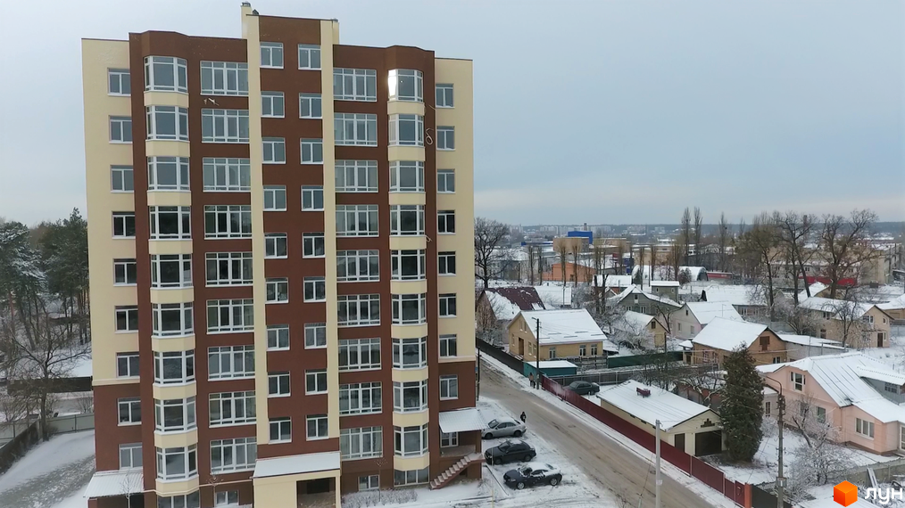 Висотна будівля ЖК Green Life-2 з коричневим фасадом та панорамними вікнами. Навколо будинку засніжена прибудинкова територія з приватними будинками.
