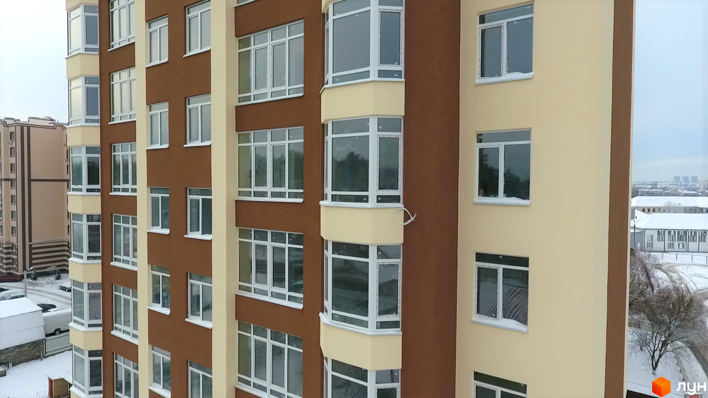 Багатоповерховий будинок ЖК Green Life-2 з панорамними вікнами та балконами. На прибудинковій території сніг, видно інші будівлі.