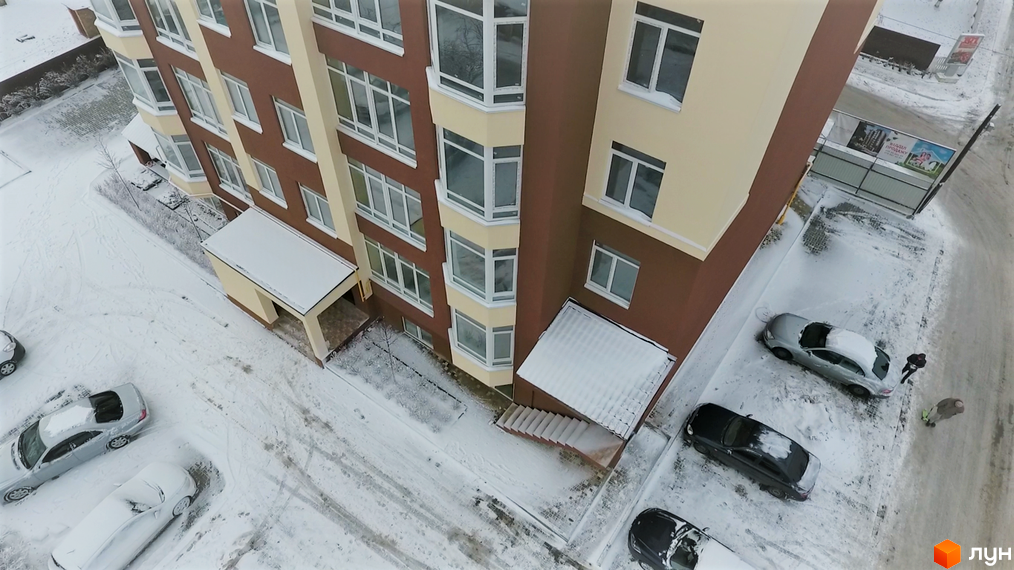 Житловий комплекс Green Life-2 з коричневими та бежевими фасадами взимку. Навколо будинку засніжена територія з припаркованими автомобілями.