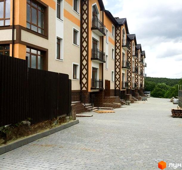 Житловий комплекс на вул. Лисеницька, 56: ряд будинків з бежево-помаранчевими фасадами, темними декоративними елементами та балконами. Територія вимощена бруківкою.