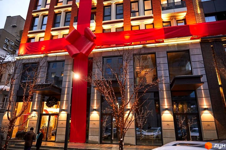 Фасад Будівельного проєкту New York Concept House, прикрашений червоною стрічкою та бантом. Перед будівлею дерева з гірляндами.