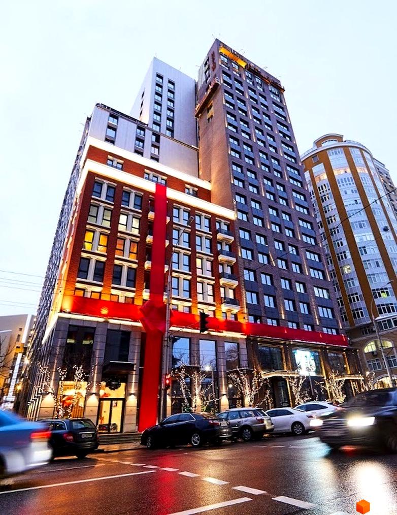 Зовнішній вигляд будівлі New York Concept House, прикрашеної великим червоним бантом. На передньому плані вулиця з автомобілями.