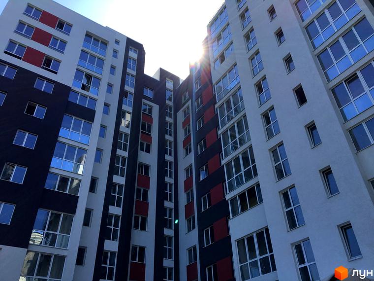 Зовнішній вигляд житлового комплексу Контраст з фасадами білого, чорного та червоного кольорів. Багатоповерхові будинки з великою кількістю вікон.