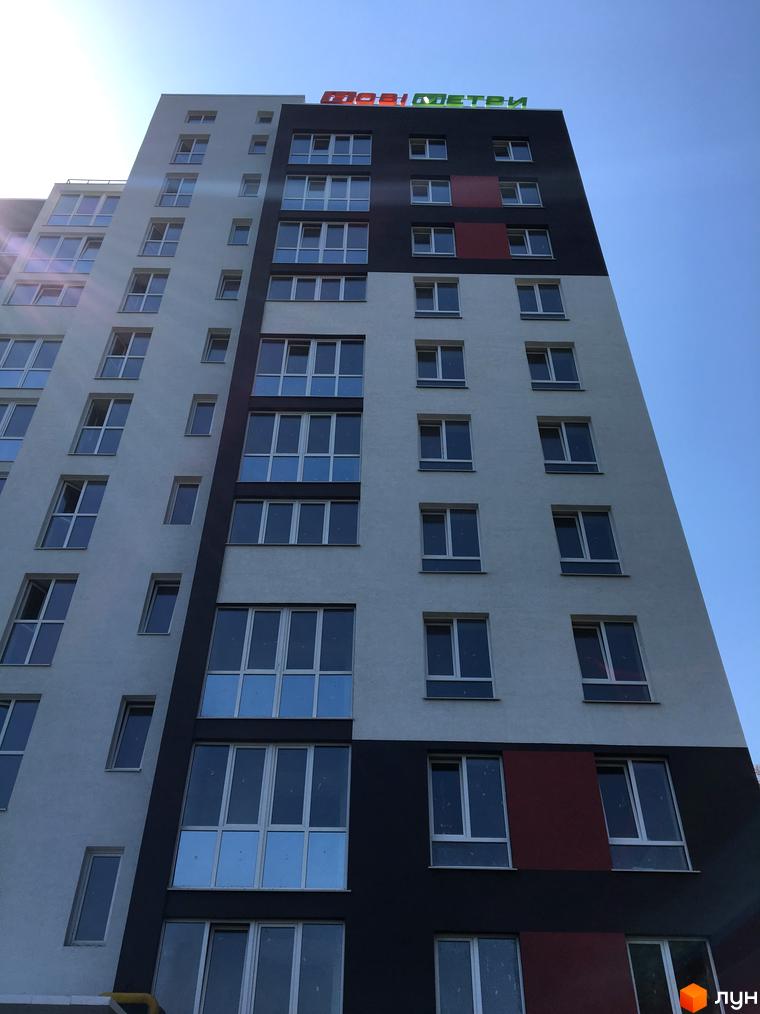 Житловий комплекс Контраст – висотна будівля з контрастним фасадом у сірих тонах та червоною вставкою. Багато вікон, блакитне небо.