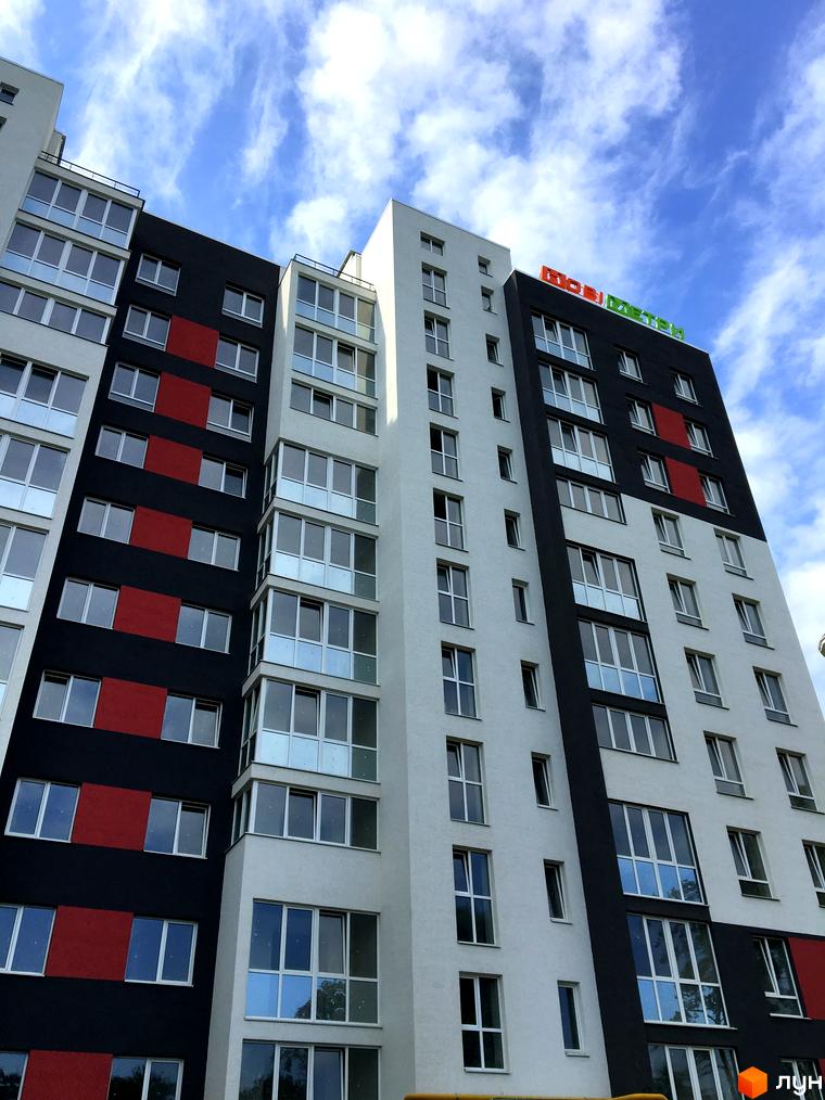 Зовнішній вигляд новобудови ЖК Контраст з чорно-білим фасадом та червоними вставками. Багатоповерховий будинок з великою кількістю вікон під блакитним небом з хмарами.