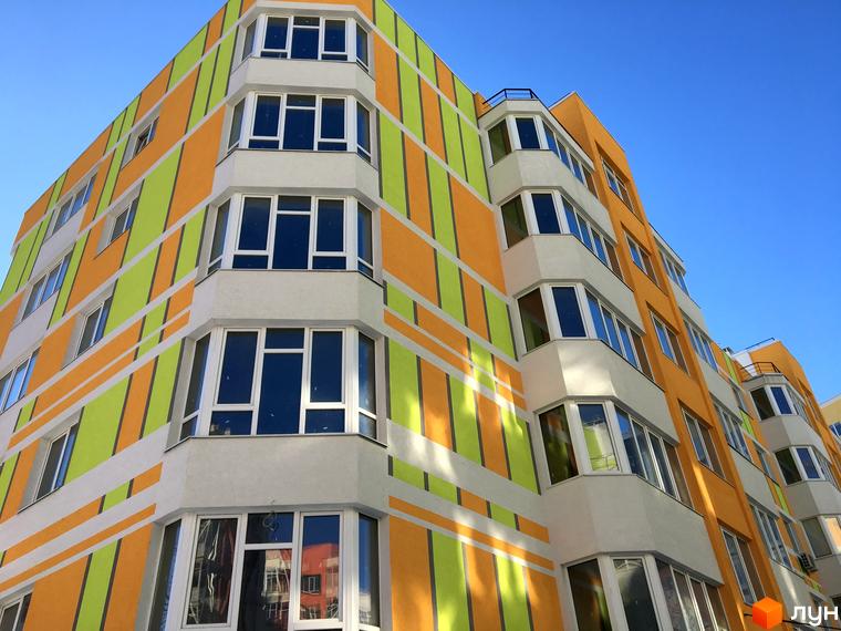 Житловий комплекс Позитив з яскравим фасадом у жовто-зелену смужку. Багатоповерховий будинок з еркерними вікнами та балконами.
