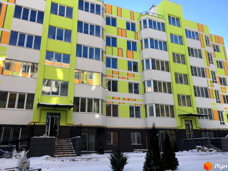Зовнішній вигляд новобудови ЖК Позитив з яскравим фасадом та вікнами. Навколо будинку засніжена територія з деревами та вхідними групами.