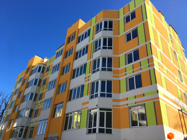 Фасад житлового комплексу Позитив з яскравим оздобленням у жовто-зелених тонах. Багатоповерхова будівля з численними вікнами та балконами.